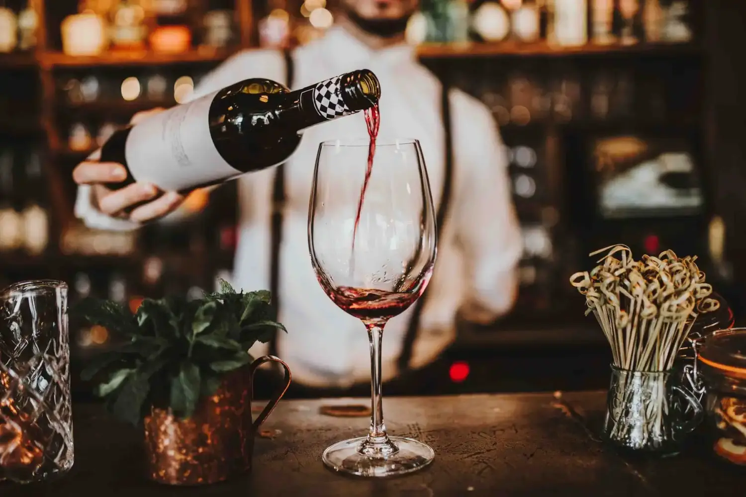  Nahaufnahme eines Barkeepers, der Rotwein in ein Glas einschenkt.